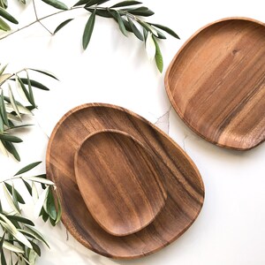 May include: Two wooden serving platters, one round and one oval, made of acacia wood. The platters are on a white background.