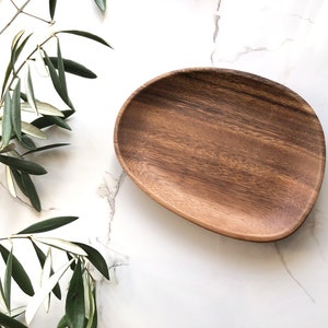 May include: A natural wood serving tray with a rounded, organic shape. The tray is made of dark brown wood with a smooth, polished finish.