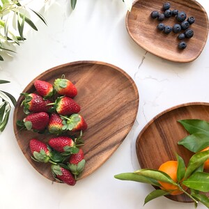 May include: Three wooden serving trays with different fruits and greenery. The first tray has red strawberries, the second has blue blueberries, and the third has orange citrus fruit with green leaves.