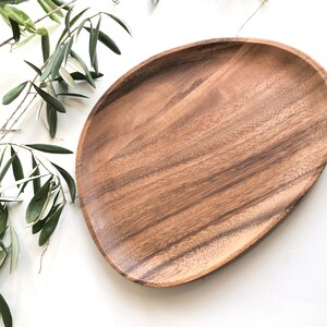 May include: A large, oval-shaped wooden serving platter with a natural wood grain finish. The platter is made of acacia wood and has a smooth, polished surface.
