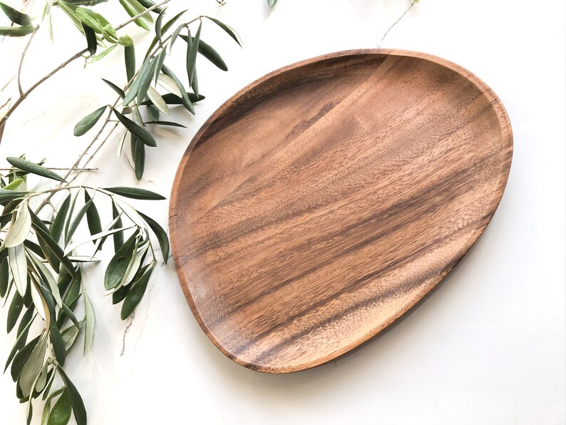 May include: A large, oval-shaped wooden serving platter with a natural wood grain finish. The platter is made of acacia wood and has a smooth, polished surface.