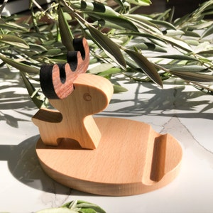 May include: A wooden phone stand shaped like a reindeer with a brown base and black antlers. The stand is designed to hold a phone upright.