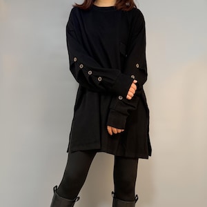 Può includere: Tunica nera a maniche lunghe con polsini abbottonati e spacco laterale. La tunica è abbinata a leggings neri e stivali neri al ginocchio. Un outfit semplice e moderno.