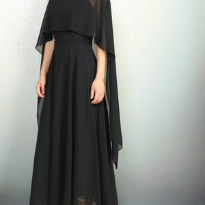 K&ouml;nnte beinhalten: Ein schwarzes Maxikleid mit einem transparenten Chiffon-Cape-&Uuml;berwurf. Das Kleid hat ein figurbetontes Oberteil und einen flie&szlig;enden Rock.