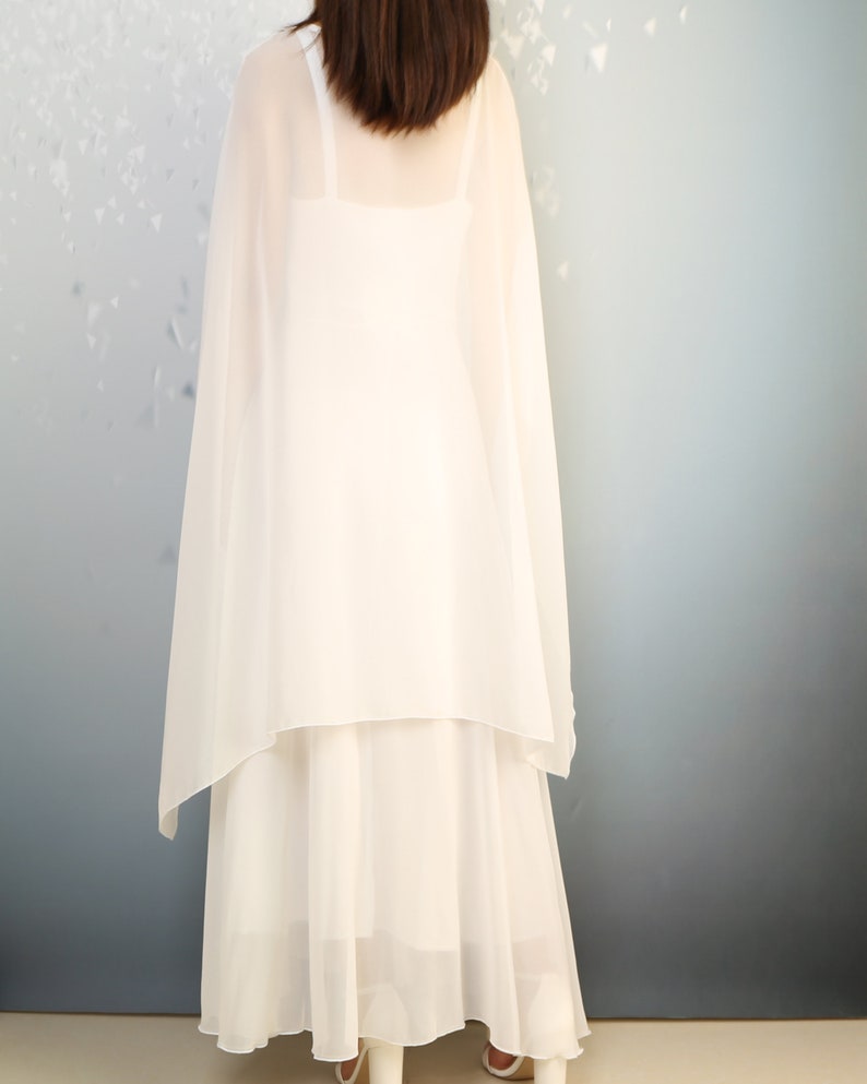 K&ouml;nnte beinhalten: Ein wei&szlig;es Chiffonkleid mit einem langen, flie&szlig;enden Rock und einer transparenten &Uuml;berlage. Das Kleid ist &auml;rmellos und hat ein schlichtes, elegantes Design.