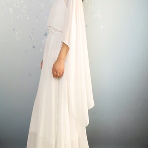K&ouml;nnte beinhalten: Ein wei&szlig;es Maxikleid mit einem flie&szlig;enden Umhang. Das Kleid hat ein schlichtes, elegantes Design und ist perfekt f&uuml;r einen besonderen Anlass.