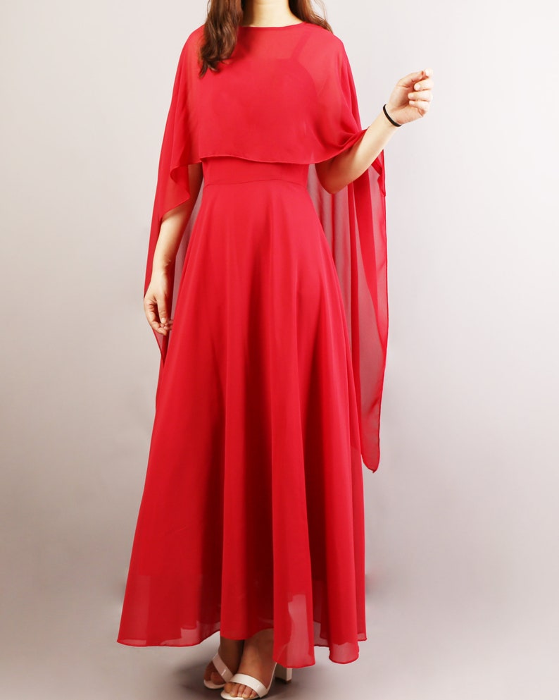 K&ouml;nnte beinhalten: Ein langes, rotes, flie&szlig;endes Maxikleid mit einem durchsichtigen Umhang dar&uuml;ber. Das Kleid hat ein tailliertes Oberteil und einen flie&szlig;enden Rock.