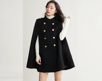 May include: A black double-breasted cape coat featuring a high collar and six round, light-colored buttons arranged in two vertical rows on the front. The garment includes shoulder epaulets with matching buttons and an open-side design.