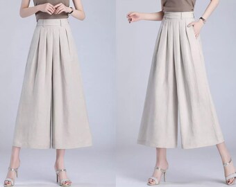 May include: A pair of wide-leg, light beige culottes with pleats in the front. The culottes are made of a lightweight fabric and have a high waist.