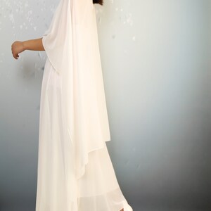 K&ouml;nnte beinhalten: Ein wei&szlig;es, flie&szlig;endes Maxikleid mit einem drapierten, asymmetrischen Design. Das Kleid ist aus einem leichten, durchsichtigen Stoff gefertigt und hat eine lockere Passform.