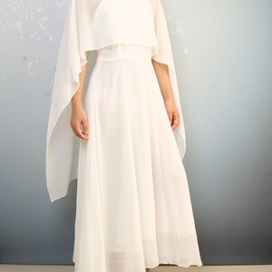 K&ouml;nnte beinhalten: Ein wei&szlig;es Maxikleid mit einem durchsichtigen Umhang dar&uuml;ber. Das Kleid hat ein tailliertes Oberteil und einen flie&szlig;enden Rock.