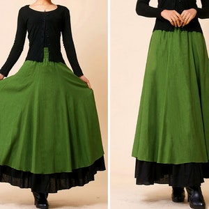 May include: A long, green skirt with a black underskirt, worn with a black long-sleeved top. The skirt has a flowing design, suitable for various occasions. The style suggests a bohemian or vintage aesthetic, with a layered effect.