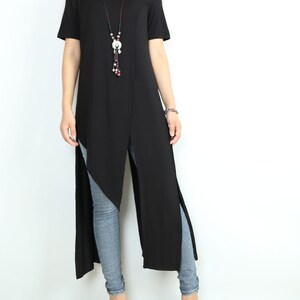 May include: A black long tunic top with side slits and a long beaded necklace. The top is worn with light blue jeans and white heels.