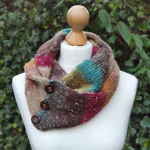 May include: A multi-colored knitted cowl with brown buttons. The cowl is made of a soft, textured yarn and has a variety of colors, including brown, pink, teal, and yellow.