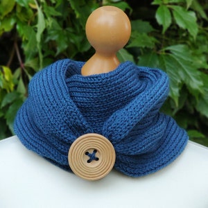 Puede incluir: Una bufanda de cuello de tortuga de punto azul con un botón de madera. La bufanda se muestra en un maniquí blanco.