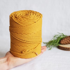 Puede incluir: Un carrete de cuerda de algodón gruesa de color amarillo. La cuerda está enrollada apretada y lista para ser utilizada en proyectos de artesanía.