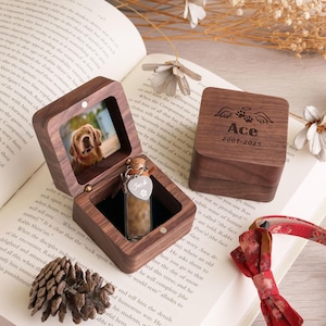 May include: A wooden pet memorial box with a photo of a golden retriever inside. The box holds a small glass vial with a heart-shaped tag that says "Jack". The box lid is engraved with "Ace 2009-2025".