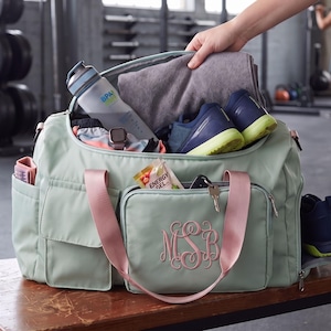 A hand is holding a gym bag filled with various items, including a water bottle, towel, and shoes, in a gym setting.
