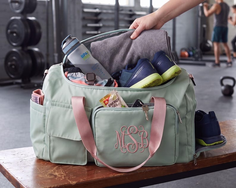 A hand is holding a gym bag filled with various items, including a water bottle, towel, and shoes, in a gym setting.