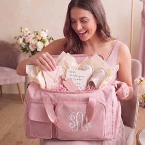 A woman in a pink dress is holding a pink bag with a personalized monogram, smiling as she looks inside the bag.