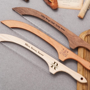 May include: Three wooden bread slicers with wire blades. One is dark brown with "Cutting Through Crusts. Creating Smiles" engraved. Another is light brown with "ER EST. 11. 28. 2024" engraved. The third is light wood with "Slice, Serve, Savor" and "RICHARD" engraved.