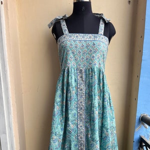 Puede incluir: Un vestido maxi azul claro con estampado floral y tirantes de lazo. El vestido tiene un frente abotonado y una falda fruncida.