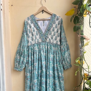 May include: A long, blue and white floral print dress with a V-neckline and long sleeves. The dress has a gathered waist and a ruffled hem.