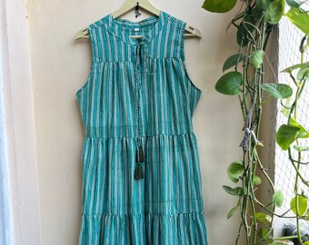 May include: A tiered maxi dress with a green and white striped pattern. The dress has a sleeveless design and a tie at the neckline.