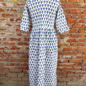 May include: White cotton dress with a blue and gray floral print. The dress has a V-neckline and 3/4 sleeves. The dress is pleated at the waist and has a flowy skirt.