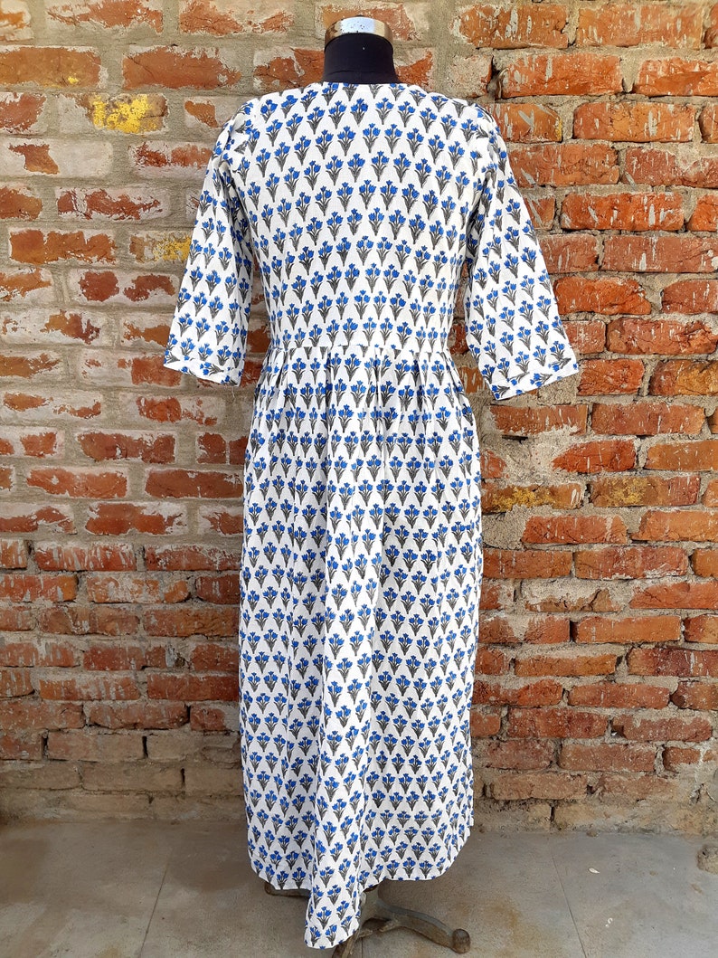 May include: White cotton dress with a blue and gray floral print. The dress has a V-neckline and 3/4 sleeves. The dress is pleated at the waist and has a flowy skirt.