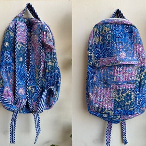 Puede incluir: Una mochila de color azul y morado con estampado floral y rayas blancas en las correas. La mochila tiene un bolsillo con cremallera en la parte delantera.