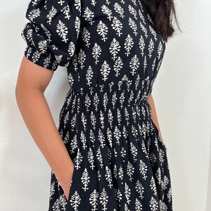 May include: A black and white cotton dress with a floral print and a smocked waist. The dress has short puff sleeves and a loose fit.