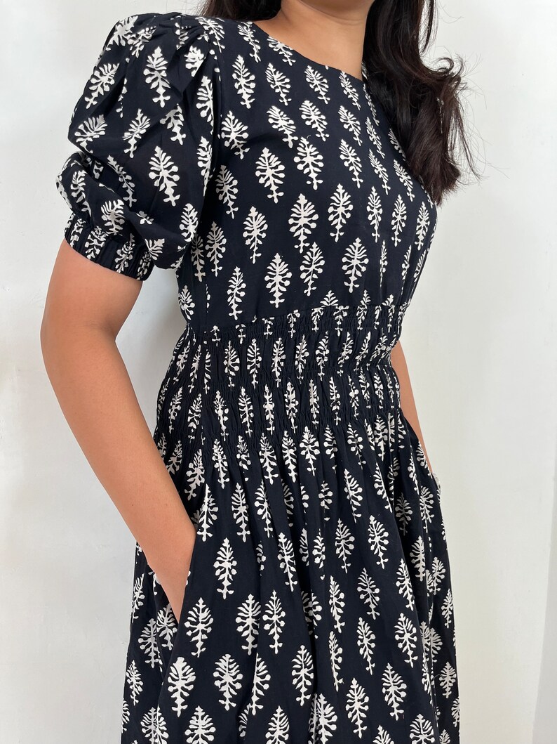 May include: A black and white cotton dress with a floral print and a smocked waist. The dress has short puff sleeves and a loose fit.