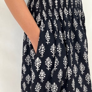May include: Black maxi dress with a white floral print. The dress has a smocked waistband and a pocket on the side.
