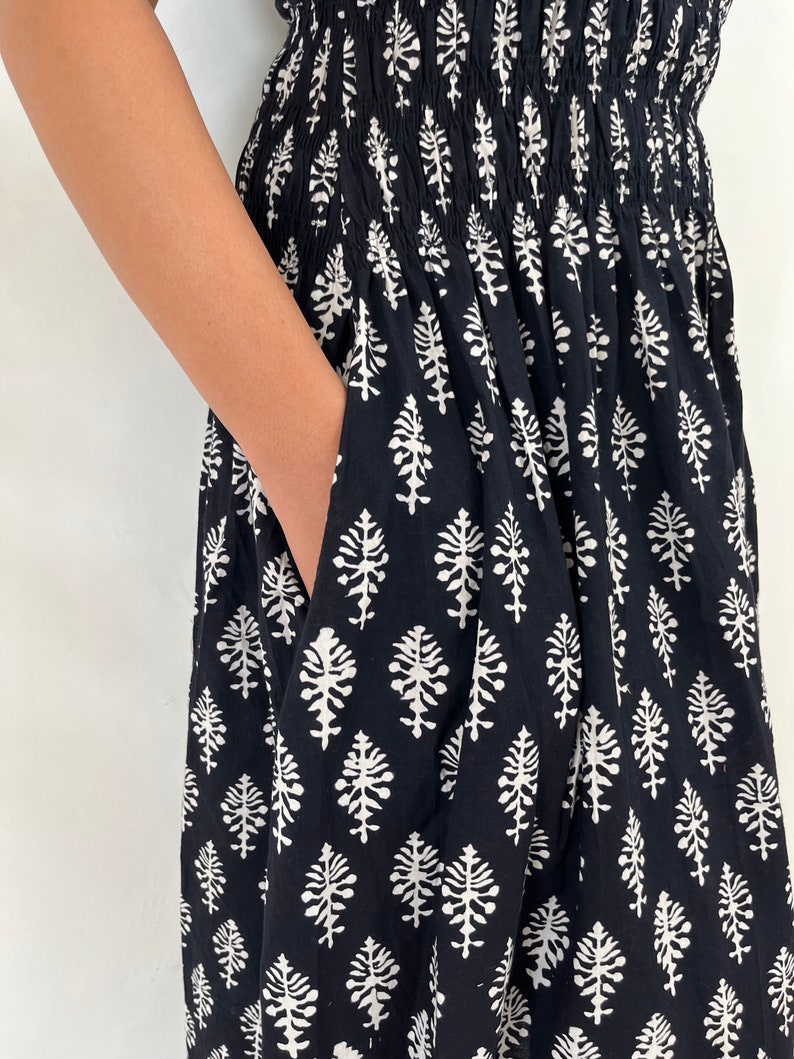 May include: Black maxi dress with a white floral print. The dress has a smocked waistband and a pocket on the side.