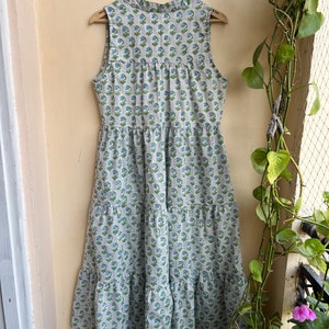 Op de afbeelding: Een mouwloze, gelaagde maxi-jurk met een bloemenprint in tinten blauw en groen op een witte achtergrond.