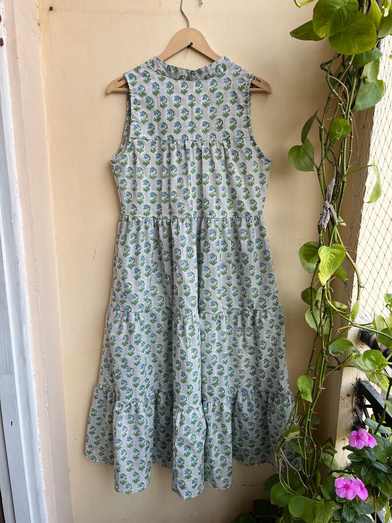 Op de afbeelding: Een mouwloze, gelaagde maxi-jurk met een bloemenprint in tinten blauw en groen op een witte achtergrond.