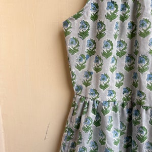 Op de afbeelding: Een mouwloze jurk met een lichtblauwe en groene bloemenprint. De jurk heeft een geplooide rok en een halternek.