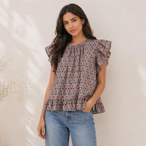 Könnte beinhalten: Ein graues Oberteil mit einem Blumenmuster in Rosa und Weiß. Das Oberteil hat Rüschenärmel und einen Rüschensaum. Das Model trägt eine blaue Jeans. Das Oberteil ist ein lässiger Stil.