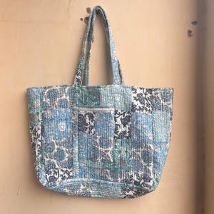 May include: A blue and white patchwork tote bag with a floral pattern. The bag has two handles and a zippered pocket on the front.