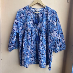 May include: A blue and white floral print top with a tie at the neck. The top has 3/4 sleeves and a loose fit.