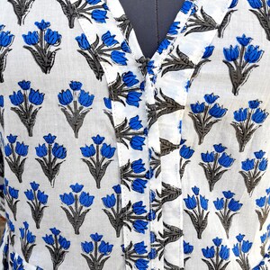 May include: White cotton fabric with a blue and gray floral print. The fabric has a V-neck and a button closure.