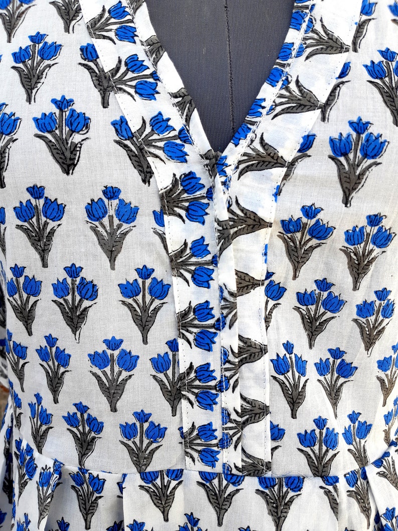 May include: White cotton fabric with a blue and gray floral print. The fabric has a V-neck and a button closure.