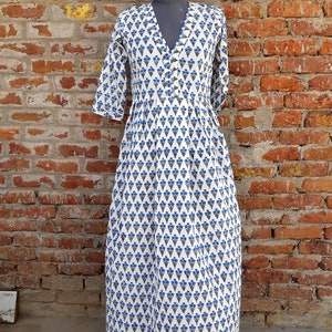 May include: A white maxi dress with a blue floral print. The dress has a V-neckline and 3/4 sleeves. It is made of cotton and has a gathered skirt.