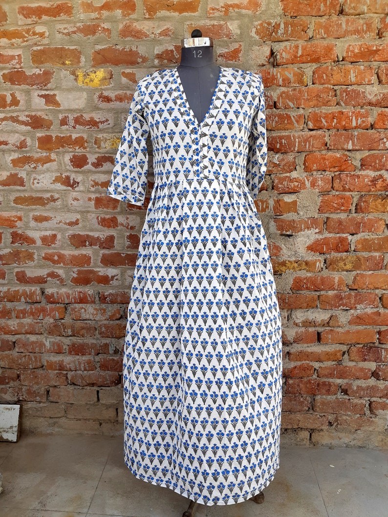 May include: A white maxi dress with a blue floral print. The dress has a V-neckline and 3/4 sleeves. It is made of cotton and has a gathered skirt.