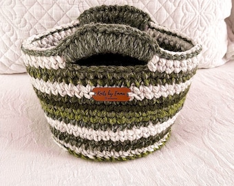 Könnte beinhalten: Ein grün-weiß gestreifter gehäkelter Korb mit zwei Henkeln. Der Korb hat ein braunes Leder-Etikett mit dem Text "Knits by Emma" darauf.