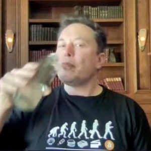 May include: A man wearing a black t-shirt with a white graphic of the evolution of humanity, ending with a Bitcoin symbol. He is holding a clear glass and drinking from it.