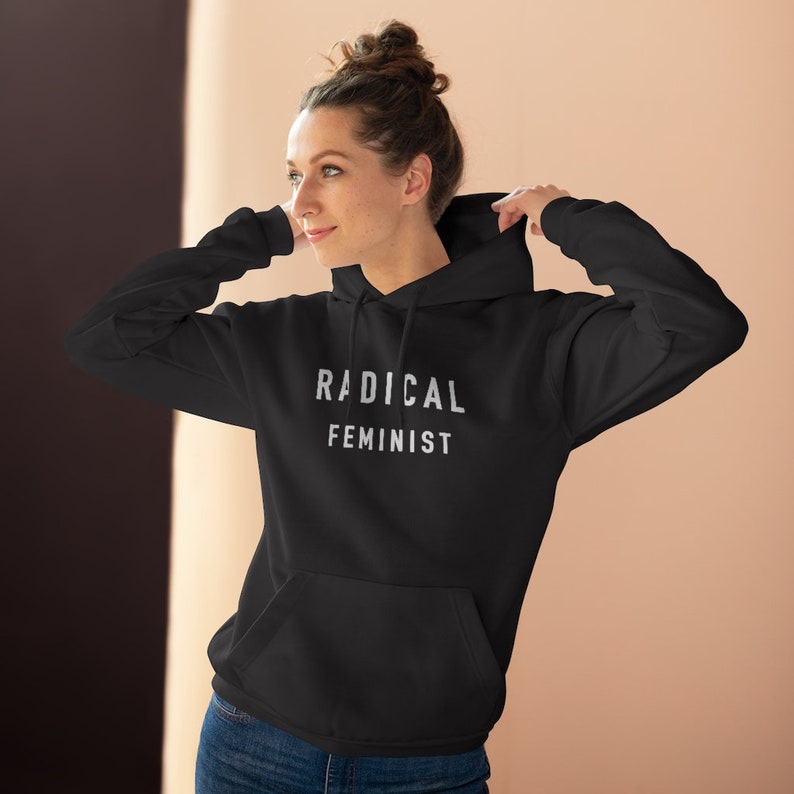 K&ouml;nnte beinhalten: Schwarzer Kapuzenpullover mit dem Text "RADICAL FEMINIST" in wei&szlig;en Buchstaben.
