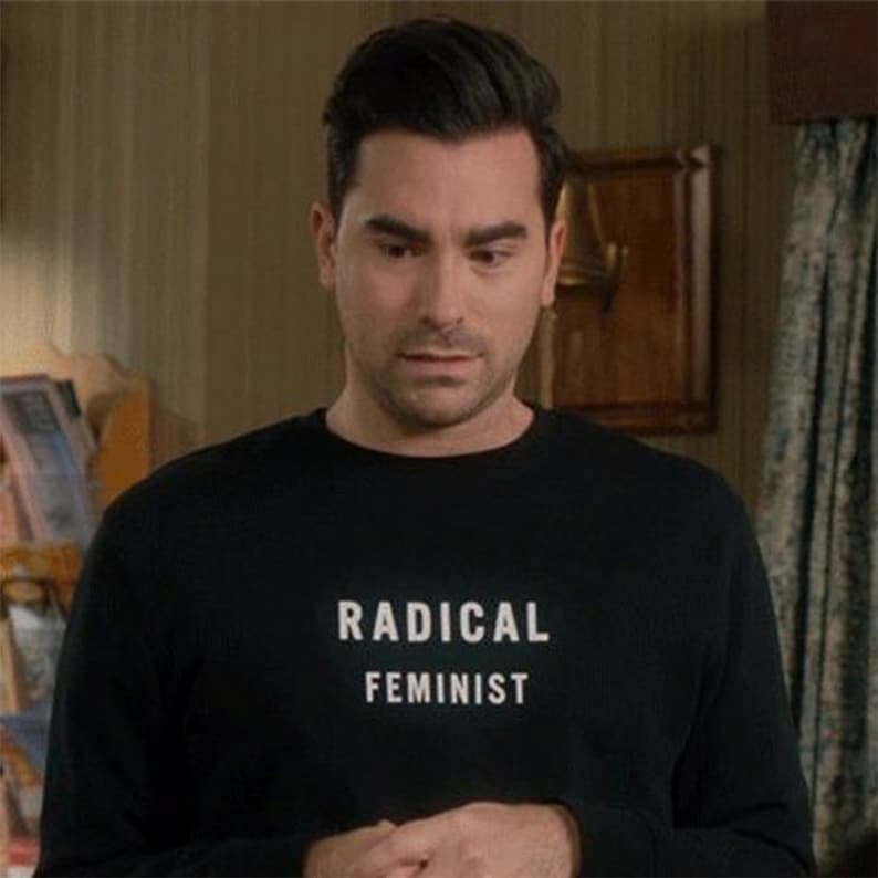 K&ouml;nnte beinhalten: Ein Mann tr&auml;gt ein schwarzes Langarmshirt mit dem Aufdruck "RADICAL FEMINIST" in wei&szlig; auf der Vorderseite.