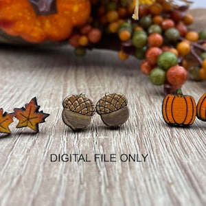 May include: A set of six wooden earrings featuring autumnal themes. The earrings are in the shape of acorns, leaves, and pumpkins. The acorns are brown with a light brown cap. The leaves are orange and yellow. The pumpkins are orange. The earrings are all small and delicate.